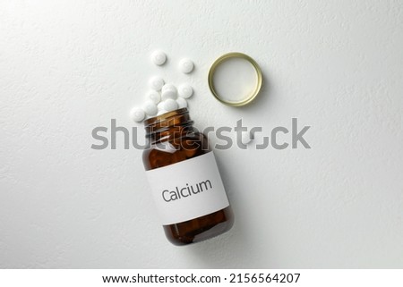 Overturned bottle of calcium supplement pills on white table, flat lay