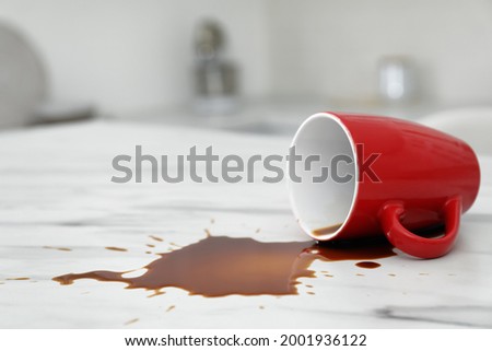 Overturned cup and spilled coffee on white marble table in kitchen, space for text