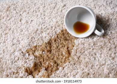 Overturned cup and spilled tea on beige carpet, closeup