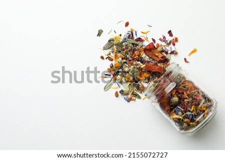 Overturned glass jar with dry herbal tea on white background, top view. Space for text