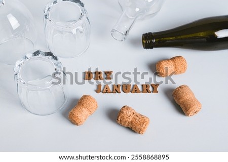 Overturned glasses, empty bottles, corks and text dry january on gray background