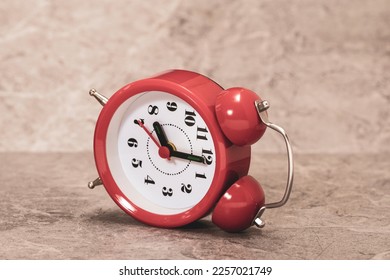 Overturned red alarm clock lying on the grey stone background - Shutterstock ID 2257021749