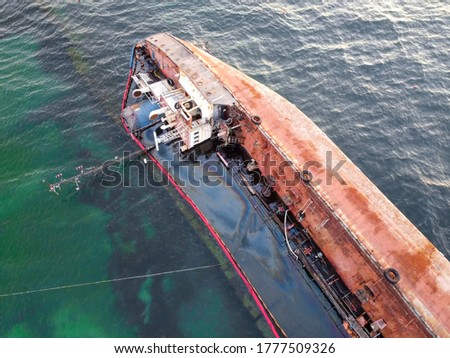 An overturned rusty tanker ran aground. Environmental disaster and oil spill into the sea by the sea. Old ship on the background of the emerald sea.