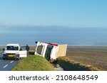 Overturned truck in a ditch in a vast agricultural landscape while the driver is waiting for help. 