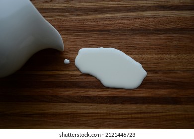 An Overturned White Milk Jug And Spilled Cream Are On A Wooden Table.