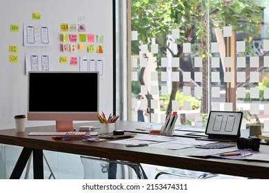 Overview Of The Busy Modern Office Decoration With Black Computer Monitor Screen Next To Any Gadgets Over Blurred Information On A Whiteboard As Background. Business And Technology Concepts.