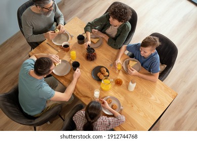 Overview Of Contemporary Family Of Five Sitting By Served Table In The Kitchen, Having Breakfast And Discussing News Or Plans For The Day