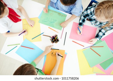 Overview Of Group Of Schoolchildren Drawing With Crayons While Sitting By Desk