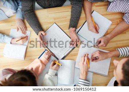 Overview of hands of students making notes and teacher answering their questions by desk