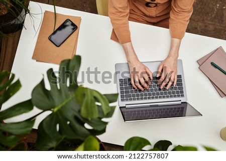 Overview of hands of young businesswoman or student typing on laptop keyboard by desk while working over presentation