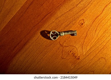 Overview Of Side Lit Antique Brass Desk Key Laid On Cherry Wood Table With Copy Space Surrounding. Side Lit Top-down View Casts Shadow And Highlights Texture.