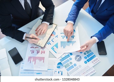 Overview of two businessmen discussing financial papers by desk while organizing work and analyzing statistics