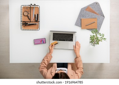 Overview of young contemporary businesswoman sitting by desk in front of laptop while going to pay by credit card for goods from online shop - Powered by Shutterstock