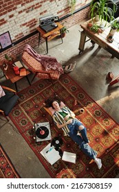 Overview Of Young Woman In Stylish Casualwear Resting On The Floor While Enjoying Music On Vynil Disks Being Played On Record Player