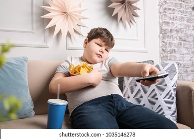 Overweight boy watching TV with snacks indoors - Shutterstock ID 1035146278