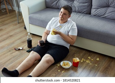 An Overweight Child Boy Enjoy Leading Unhealthy Passive Lifestyle, Sits On The Floor Watching Tv And Eating, He Moves A Little That Is Why He Is Fat