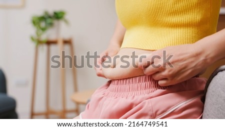 overweight concept - close up of woman hand pinching excessive belly fat in living room