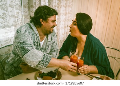 Overweight Couple Eating Healthy Food, Caucasian Man And Woman Clinking Glasses With Orange Juice While Looking At Each Other, Woman Stretched Out Her Lips For A Kiss