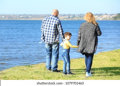 Overweight Couple With Son Walking Near River On Sunny Day