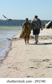 An Overweight Couple Walking Hand In Hand On The Beach.