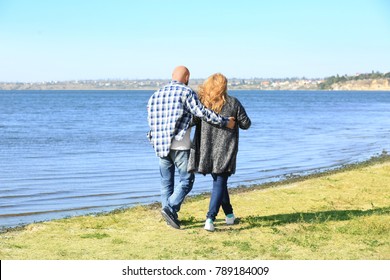 Overweight Couple Walking Near River On Sunny Day