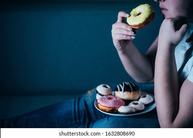 Overweight Depressed Woman Laying On Sofa Eating Sugary Food Watching TV. Sugar Addiction, Unhealthy Lifestyle, Weight Gain, Dietary, Healthcare And Medical Concept.