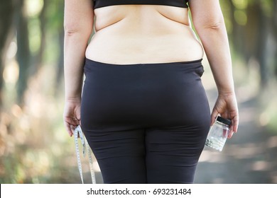 Overweight fat woman with measuring tape and slimming pills, view from the back . Weight loosing, desperate, diet, fat burning, pharmacy, medicine concept