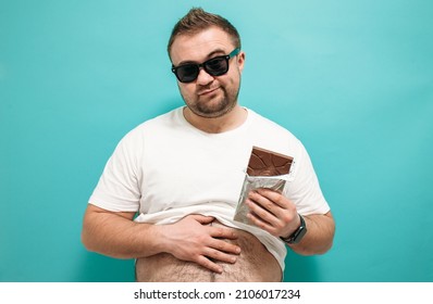 Overweight funny man biting large of chocolate with pleased joyful look. Glutton. Excessive sugar intake