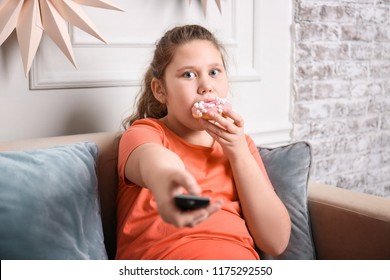 Overweight girl eating doughnut while watching TV indoors