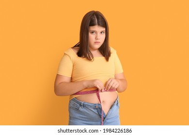 Overweight girl measuring her waist on color background