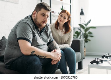 overweight girlfriend looking at sad boyfriend at home