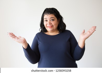 Overweight Latin Woman With Shrug Gesture Asking Something And Looking At Camera. Portrait Of Cheerful Hispanic Woman With Do Not Know Gesture. Isolated On White. Question Concept