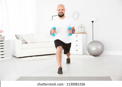 Overweight Man Doing Exercise With Dumbbells At Home