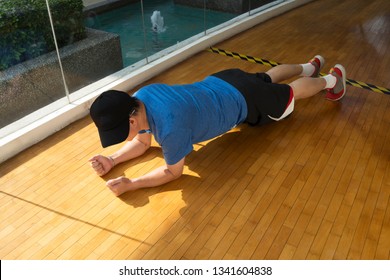 Overweight Man Doing Plank Exercise In A Gym With Wooden Floor By A Pool - Horizontal 