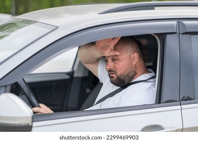 Overweight man drives in car without air conditioning in hot summer weather. Male wiping sweat from forehead suffering from heat stuffiness. Broken air conditioner. Tired exhausted overheated man.