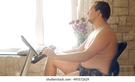 Overweight Man Exercising On Bike Simulator With Bare-chested At Home