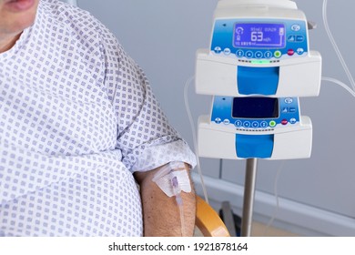 Overweight Man Sitting In A Chair With A Dropper, Equipment In The Foreground, Patient In Hospital.