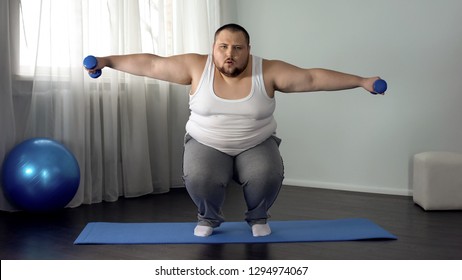 Overweight Man Squatting And Lifting Dumbbells On Mat, Full Body Training Home