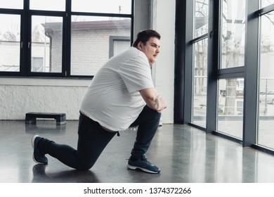 Overweight Man Stretching Legs At Sports Center With Copy Space