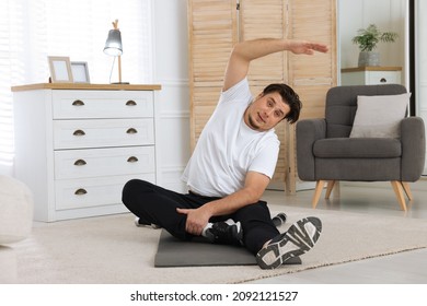 Overweight Man Stretching On Mat At Home