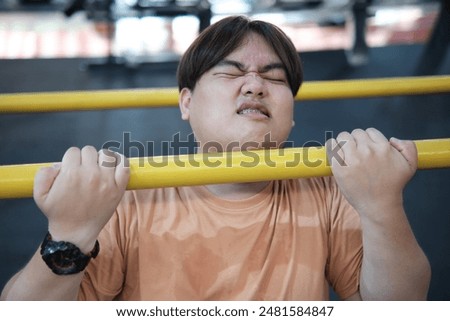 Overweight man struggling to do pull-ups in the gym, showing effort and determination.