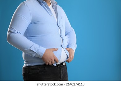 Overweight man in tight shirt on light blue background, closeup. Space for text
