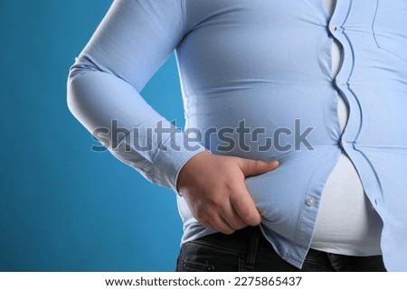 Overweight man in tight shirt on light blue background, closeup
