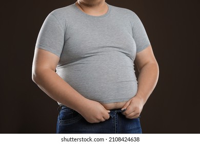 Overweight Man Trying To Button Up Tight Jeans On Dark Brown Background, Closeup