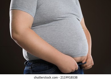 Overweight Man Trying To Button Up Tight Jeans On Dark Brown Background, Closeup