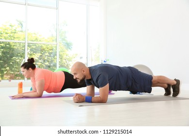 Overweight Man And Woman Doing Plank Exercise On Mats In Gym