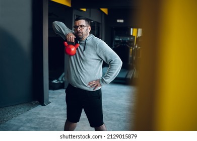 Overweight middle aged men training in the gym while using kettlebell. Overweight man trying to lose weight. Warming up.