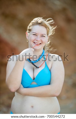 Overweight middle aged woman at the sea. Overweight woman in blue bikini bites the shackle of glasses