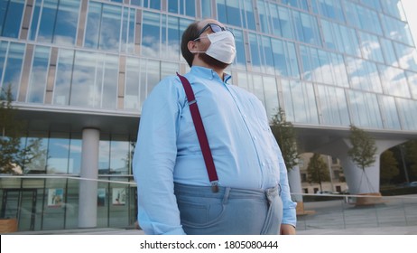 Overweight office employee tired of wearing safety mask outdoors. Portrait of obese businessman standing near office building in facial mask - Shutterstock ID 1805080444