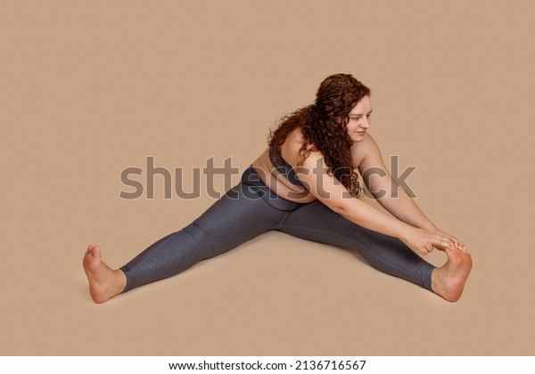 Overweight smiling enjoying woman, with\
obesity, excess fat in gray sportswear. Tummy, belly flabs incline\
to leg. Weight loss. Self challenge goal to dieting, body\
sculpting. Beige\
background